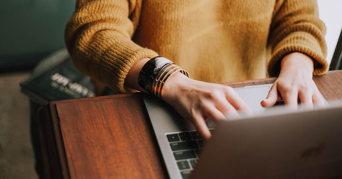 A person in a yellow sweater looks for ways to make money online on a laptop