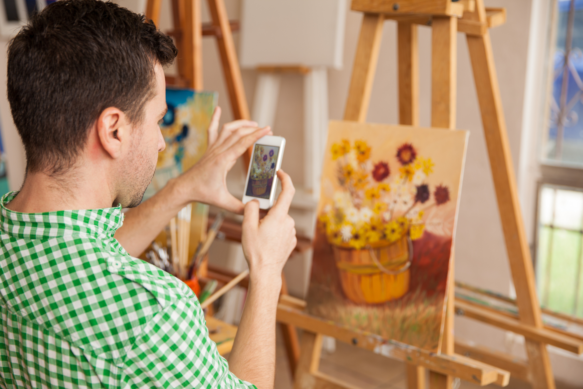 Young male artist taking a photo of his artwork with a smartphone to share it on a social network and sell it online